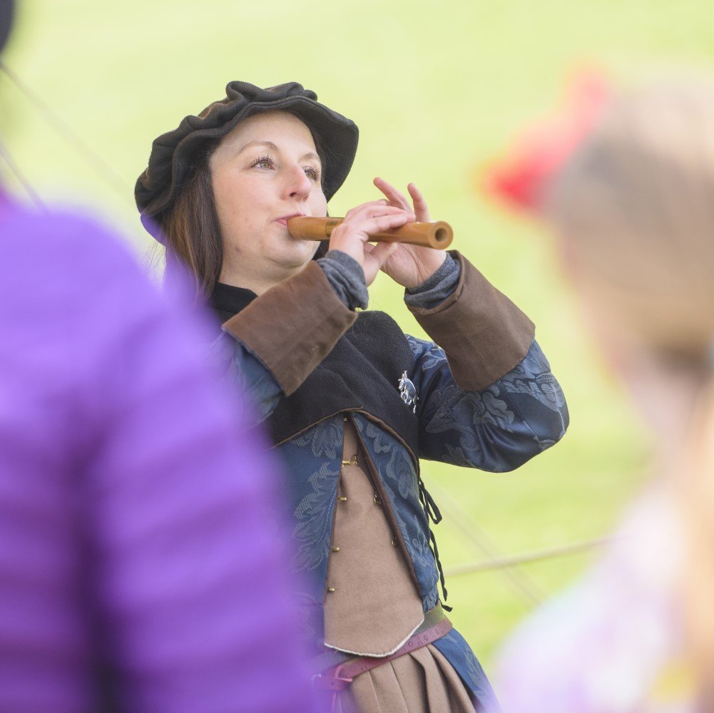 Photo of someone in medieval clothing playing a wooden recorder