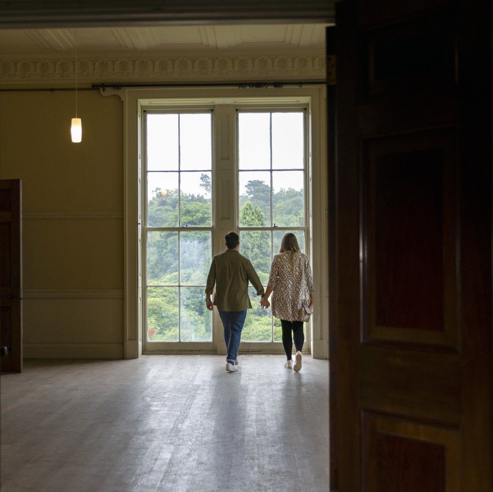 Photo of two people holding hands and walking towards a full-size window in Belsay Hall