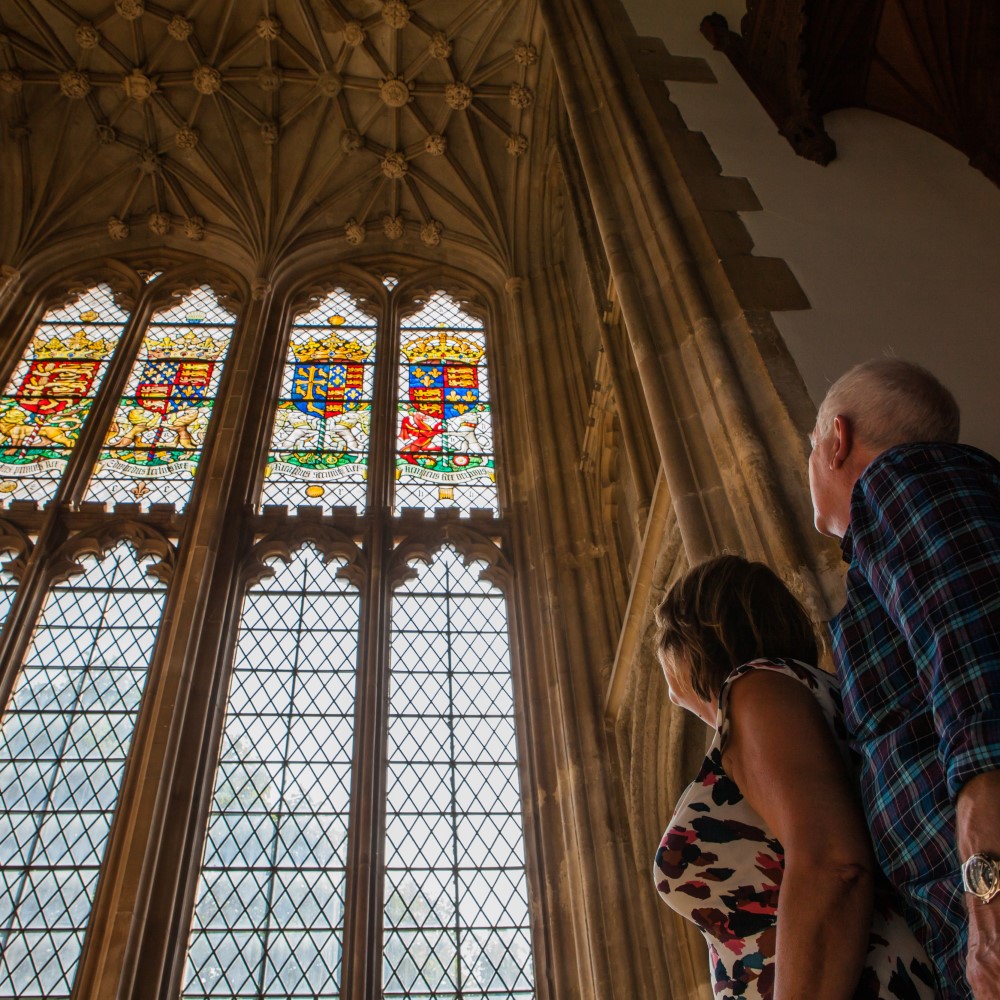 Photo of two people looking up at stained-glass windows and a vaulted ceiling at Eltham Palace