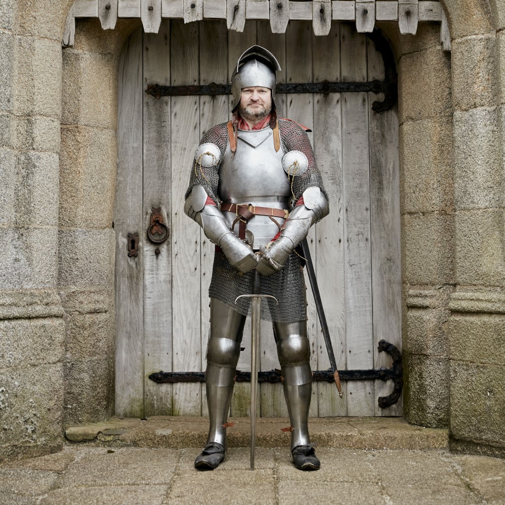 Photo of someone dressed as a Tudor knight standing in front of a medieval doorway