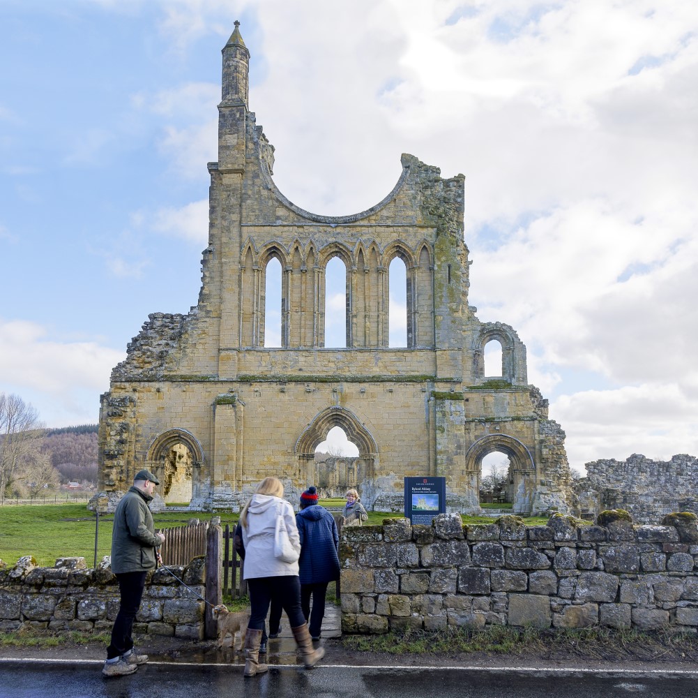 Photo of a group of people walking through the entrance gate in front of the remains of Byland Abbey