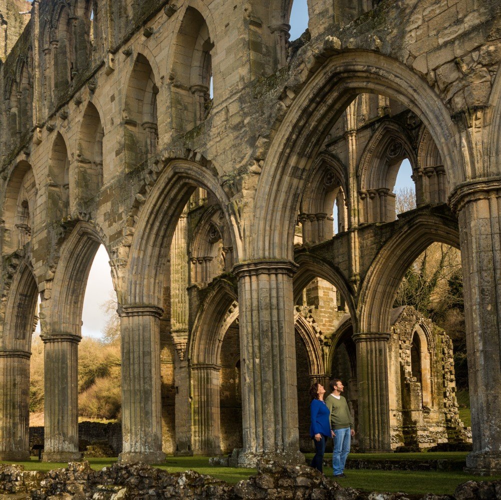 Photo of two people walking through the remains of Rievaulx Abbey