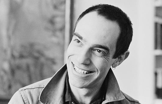 Black and white portrait photograph of Derek Jarman, smiling