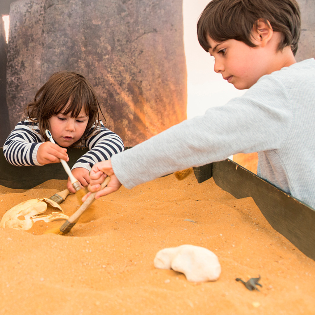 two children using brushes to dig in a sandpit